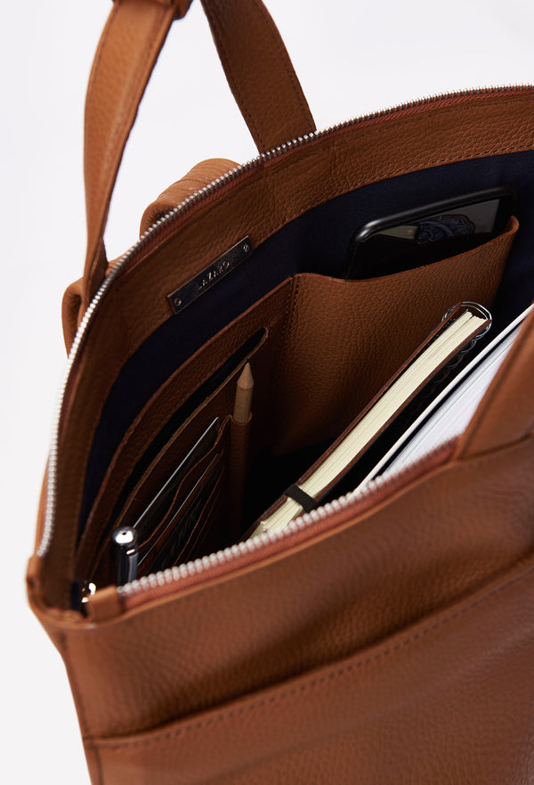 Interior of a Tan Leather Tote Backpack that shows a zippered main compartment, a front zippered pocket and an internal cell phone pocket and card holder.