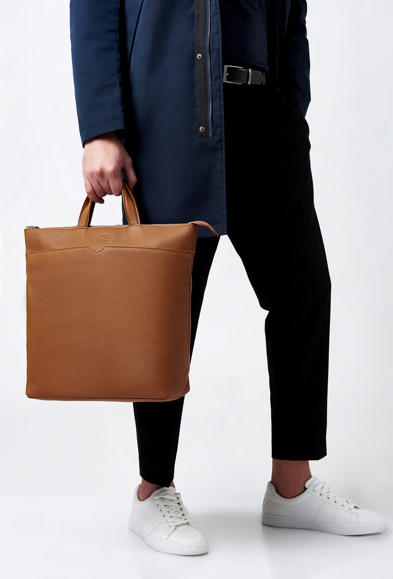 A model carries a sophisticated tan leather tote style backpack, showcasing its sophisticated design. The bag features external and internal multifunctional zippered pockets, adding to its elegant appeal. The model confidently displays the bag's size and craftsmanship while exuding a sense of style and elegance.