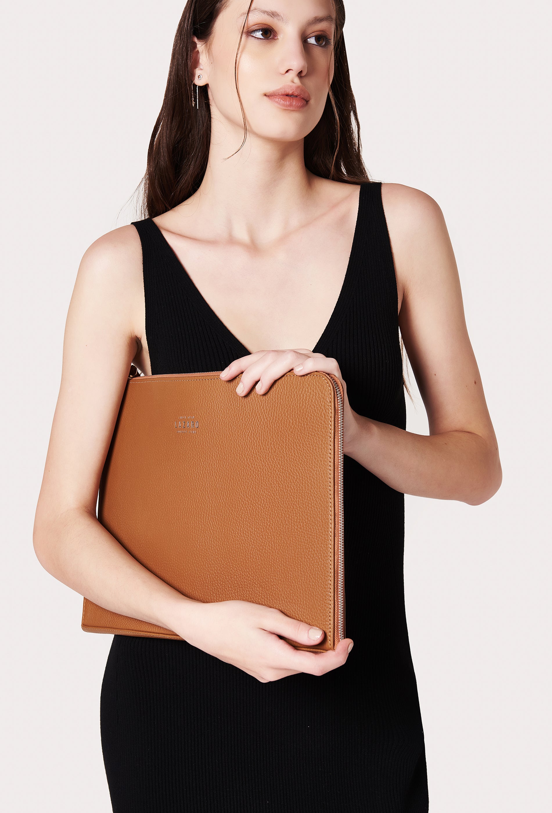 A model carries a sophisticated tan leather slim computer case, showcasing its sophisticated design. The bag features internal pockets and compartments, adding to its elegant appeal. The model confidently displays the bag's size and craftsmanship while exuding a sense of style and elegance.