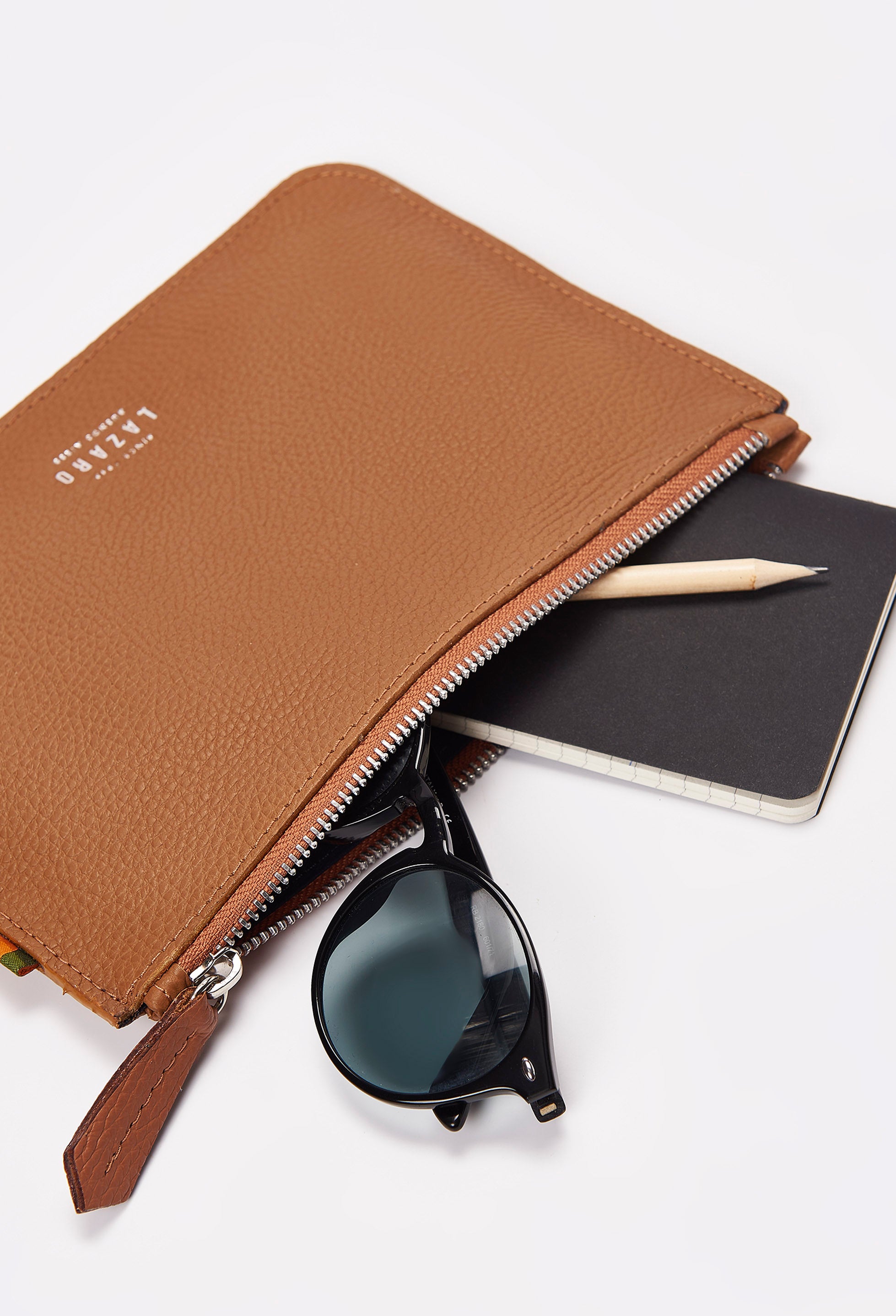 Interior of a Tan Leather Zipper Pouch packed with a notebook, a pencil and sunglasses.